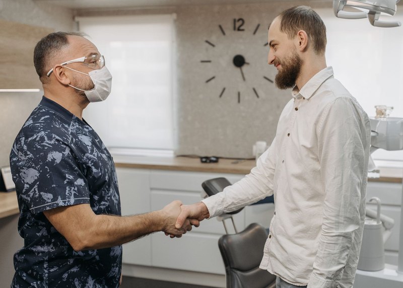Zahnarzt begrüßt eine neue Kollegin per Handschlag im Behandlungszimmer